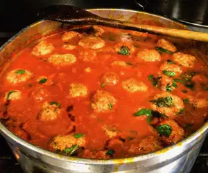 A large pot of simmering meatballs and sauce. 